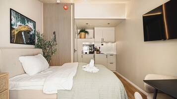 Een moderne hotelkamer met een bed, bureau, stoel, televisie en kitchenette.