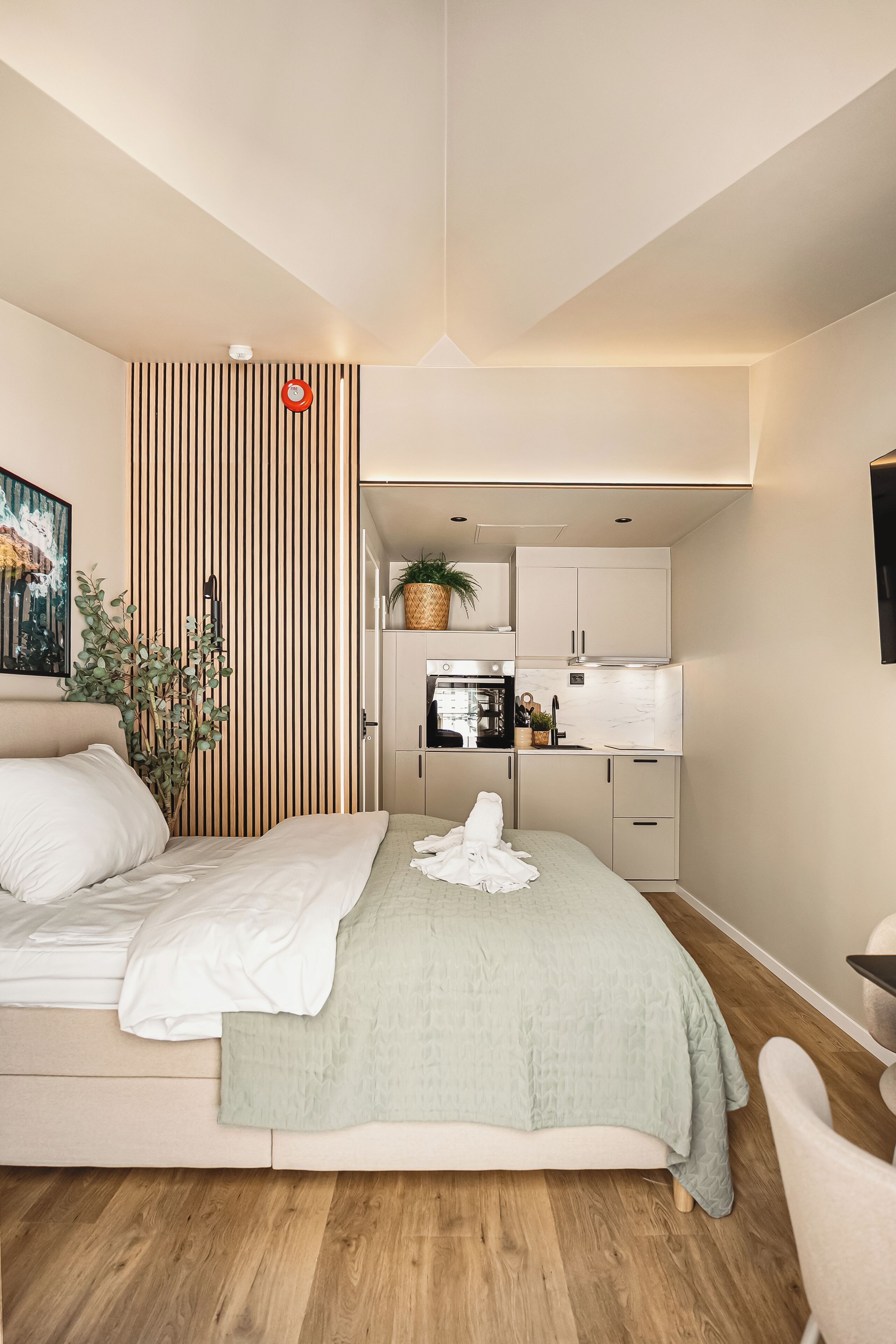 Un dormitorio moderno con una cama, una mesita de noche, una silla y vistas a una cocina con armarios y electrodomésticos.