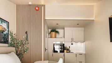 Un dormitorio moderno con una cama, una mesita de noche, una silla y vistas a una cocina con armarios y electrodomésticos.