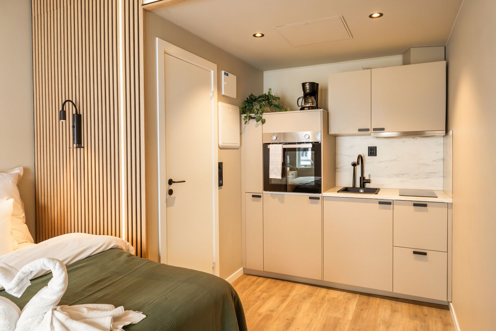 A compact hotel room with a bed, a kitchenette, and a sliding door.