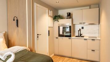 A compact hotel room with a bed, a kitchenette, and a sliding door.