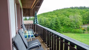 A balcony with a table and chairs, overlooking a forested hillside.