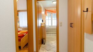 A narrow hallway leading to a bedroom with a bed, a radiator, and a window with curtains.