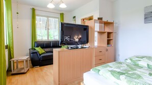 Una stanza con un letto, una televisione su un mobile in legno, un tavolino e una tenda verde.