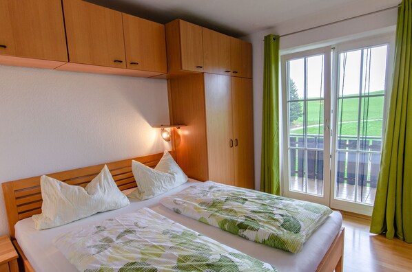 A double bed with a green leaf pattern bedspread, wooden headboard, and two pillows.