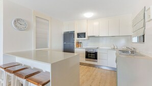 A modern kitchen with white cabinetry, a stainless steel refrigerator, an oven, and a microwave. There is a wooden island with a sink and a clock on the wall.
