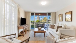 A living room with a sofa, a coffee table, a TV, and a balcony with a view of buildings.