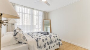 A bedroom with a bed, a nightstand, a lamp, and a large window with sheer curtains.