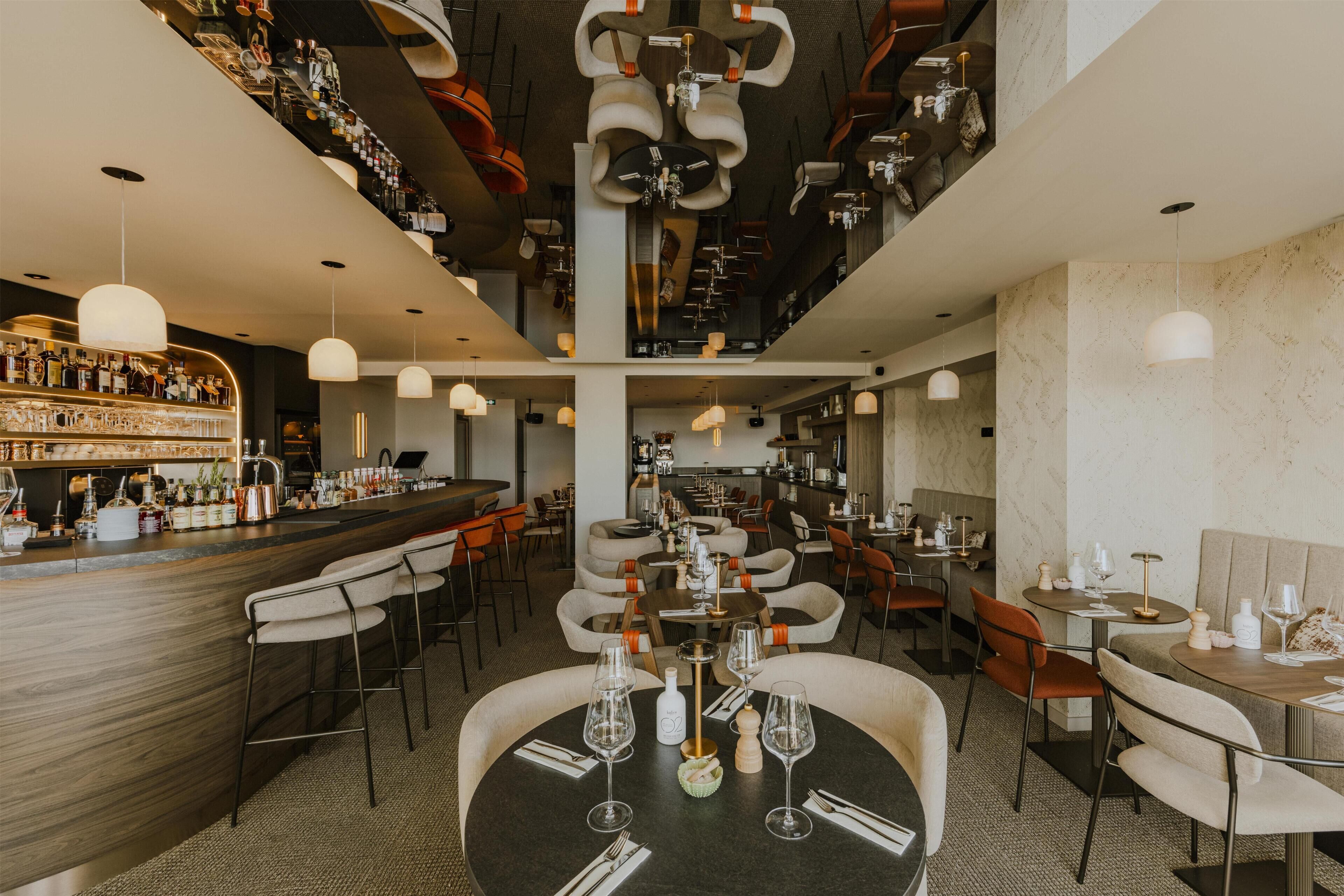 A restaurant with multiple dining tables, chairs, and a bar area with bottles and glasses.