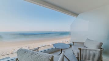 Un balcón con vista a la playa, dos sillas, una mesita redonda y una barandilla blanca.