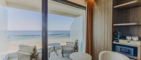 A balcony with a view of the beach, a seating area with chairs and a table, and a built-in shelf with a coffee maker and glasses.