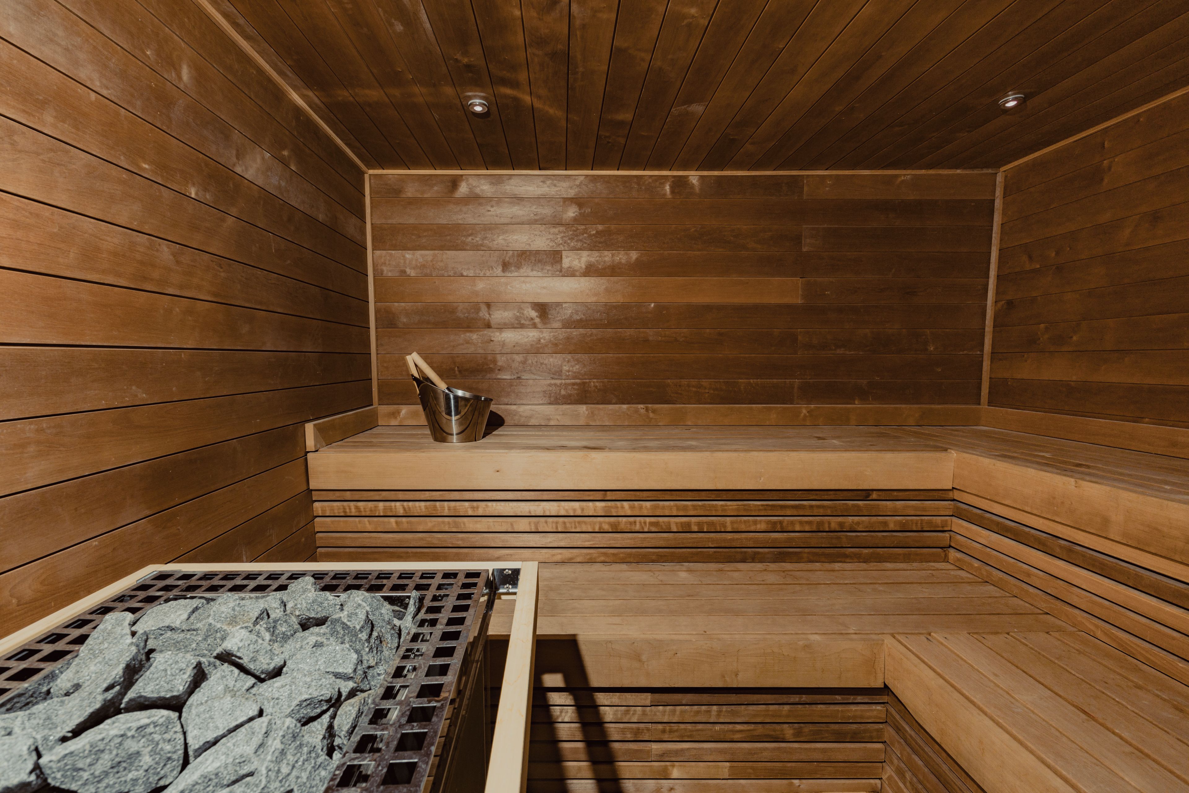 Uma sauna com paredes e bancos de madeira, um banco de metal e um recipiente metálico no banco.