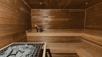 Uma sauna com paredes e bancos de madeira, um banco de metal e um recipiente metálico no banco.