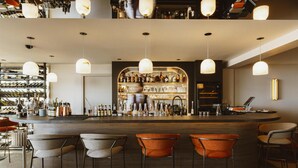 Zona de bar con mostrador, varias luces colgantes y una variedad de botellas y vasos.