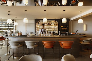 A bar area with a counter, multiple hanging lights, and a variety of bottles and glasses. - Hotel & Spa Amoria La Baule, A Member Of Radisson Individuals (La Baule-Escoublac)