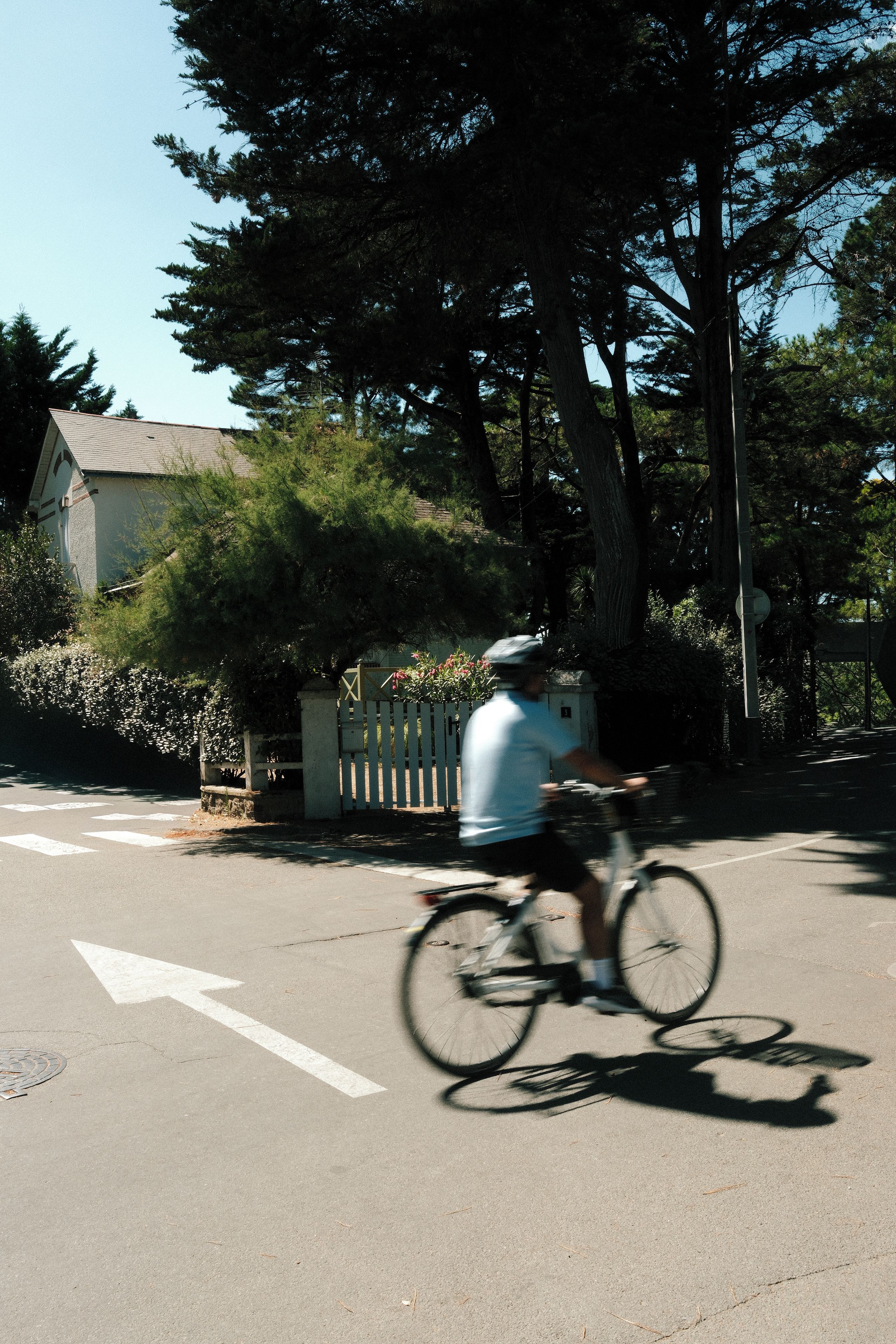 En cyklist kører ad en vej med træer og et hus i baggrunden.