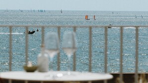 Vista al mar desde un balcón con barandilla, una mesa, un vaso y una silla.