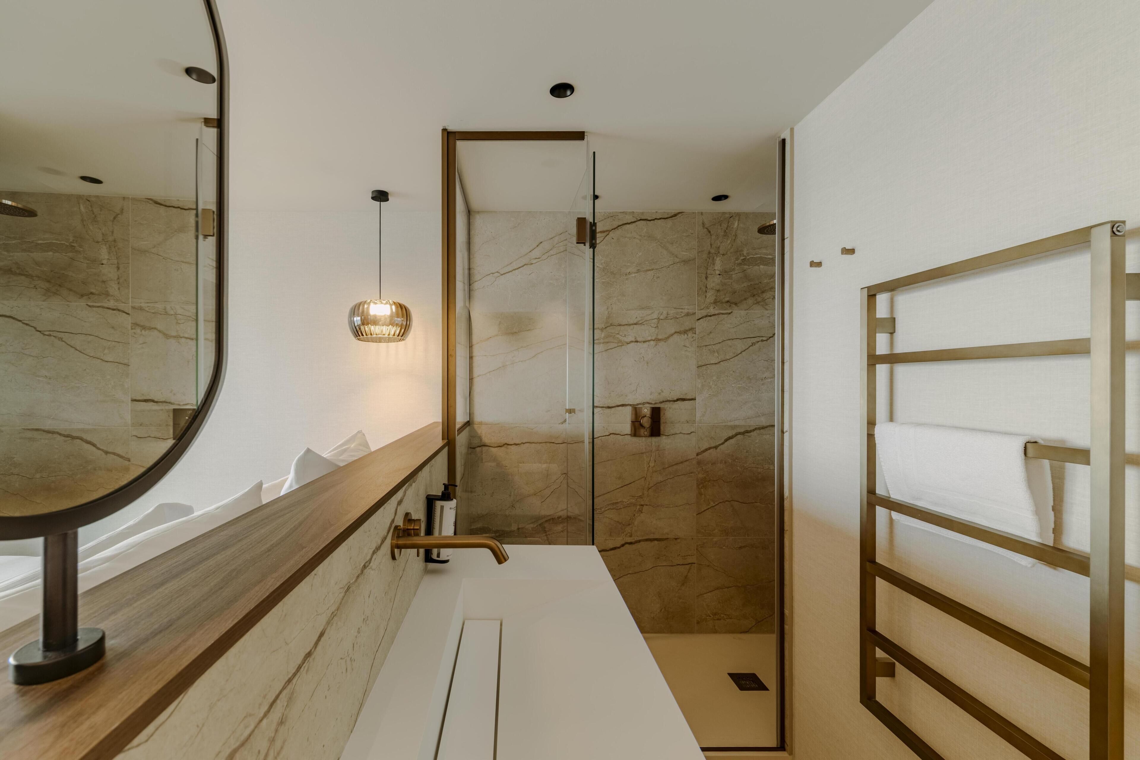 Un baño moderno con pared de mármol, tocador de madera, cabina de ducha de vidrio y un perchero para toallas.