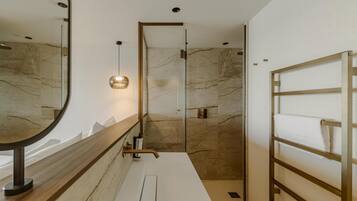 Un baño moderno con pared de mármol, tocador de madera, cabina de ducha de vidrio y un perchero para toallas.