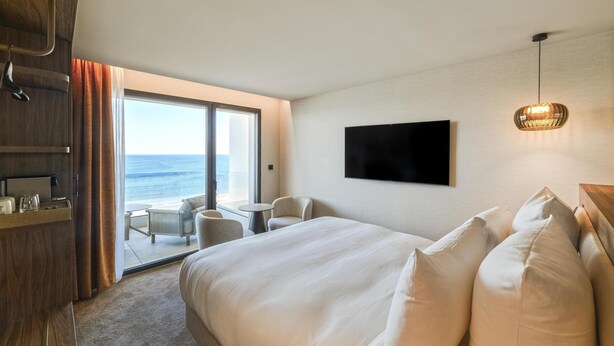 Una habitación de hotel con cama, televisión, escritorio y silla, y vistas al océano.