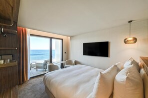 Una habitación de hotel con cama, televisión, escritorio y silla, y vistas al océano.