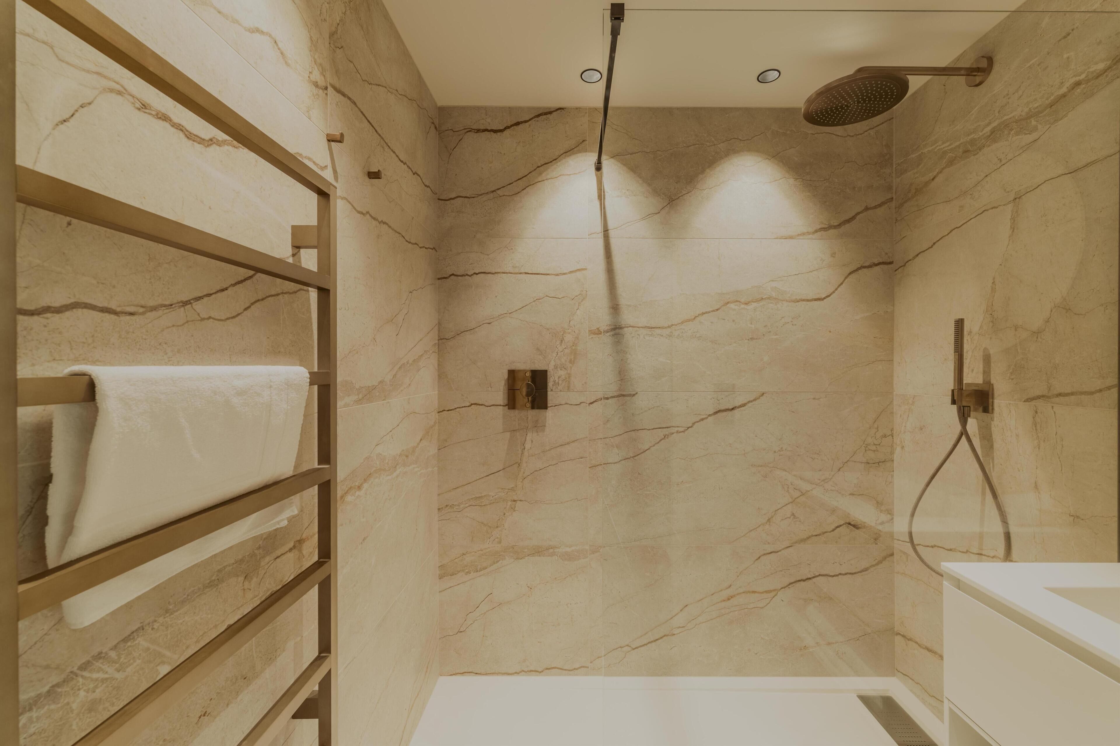 Ein modernes Badezimmer mit Marmorwänden, einer integrierten Dusche und einem Holzboden mit Handtüchern.