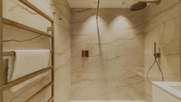 Ein modernes Badezimmer mit Marmorwänden, einer integrierten Dusche und einem Holzboden mit Handtüchern.