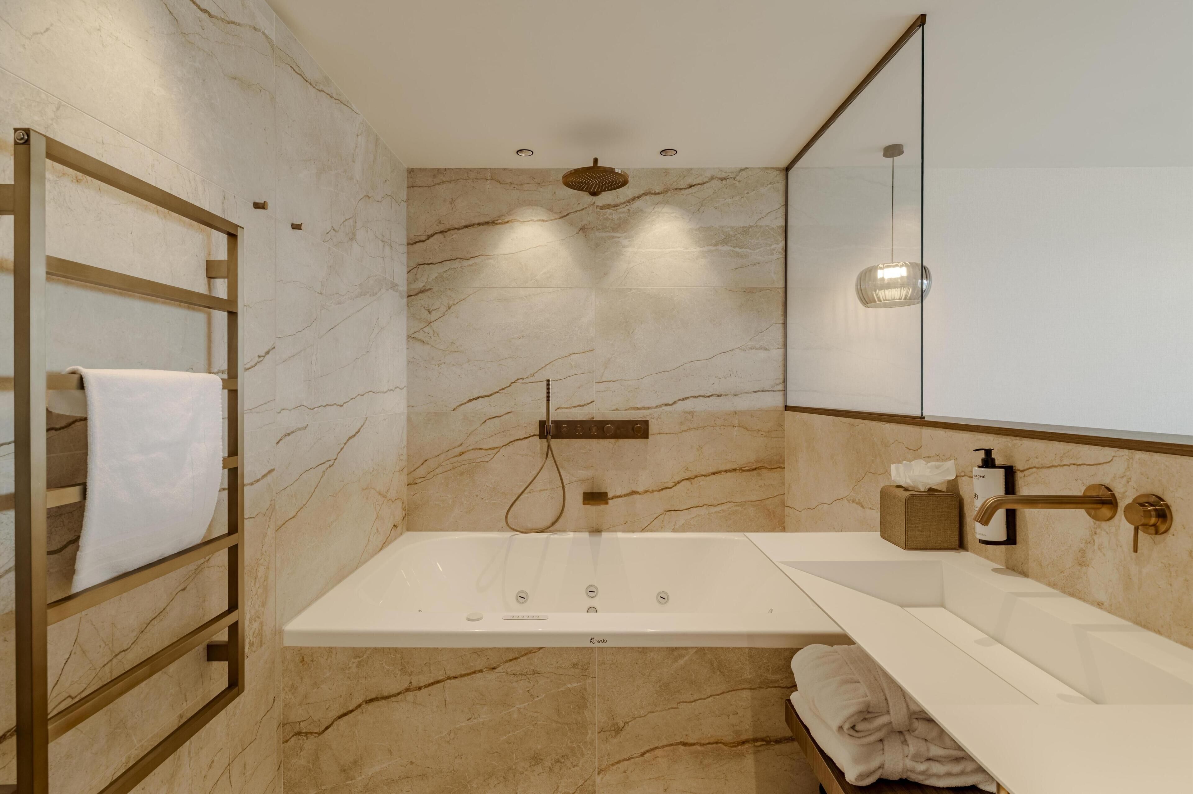 Een moderne badkamer met een marmeren wand, een inloopdouche, een grote spiegel en een handdoekrek.