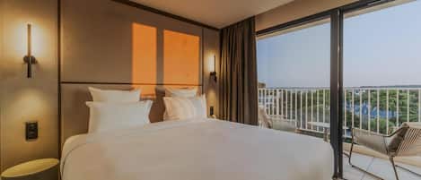 Une chambre d’hôtel avec un grand lit, une vue sur la ville et un balcon aménagé avec du mobilier d’extérieur.
