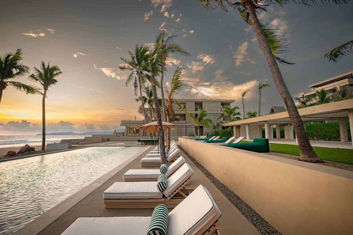 A poolside area with lounge chairs and palm trees, overlooking the ocean.