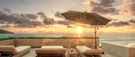 Eine Strandlounge mit Sonnenuntergangsblick, inklusive Liegestühle, einem Tisch mit Kerze und einem Sonnenschirm.