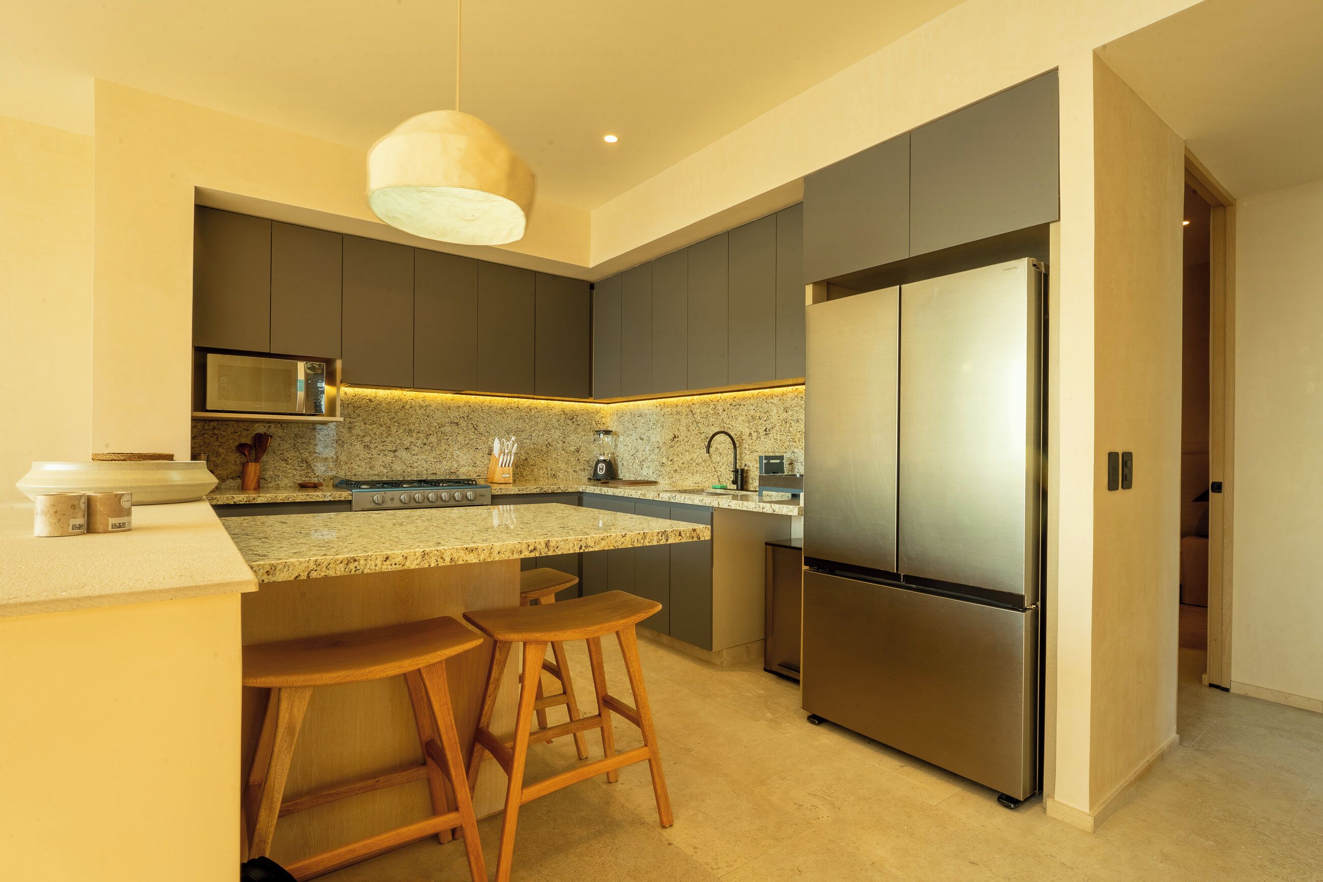 A modern kitchen with dark cabinets, a stainless steel refrigerator, and a granite countertop.