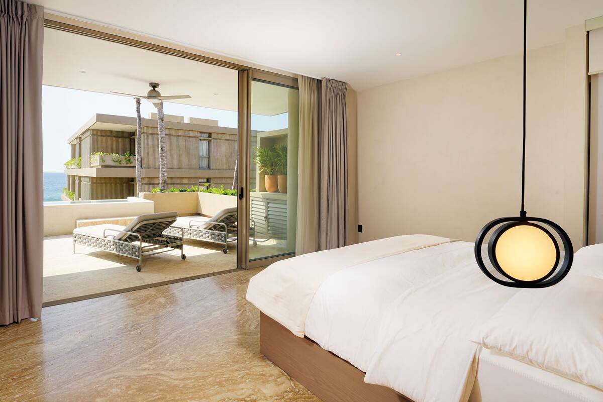 A modern hotel room with a large bed, a balcony with a chair, and a view of the ocean.