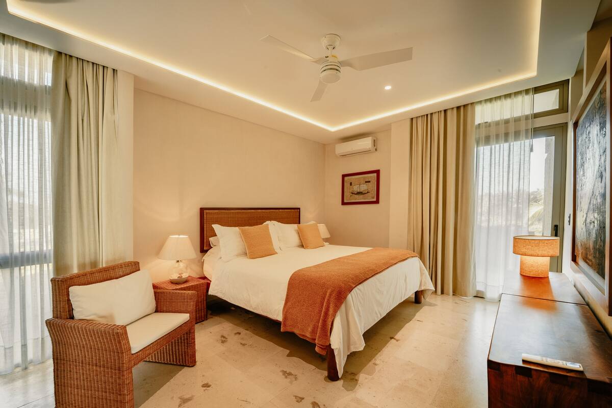 A hotel room with a bed, a chair, a nightstand, a lamp, and a painting on the wall.