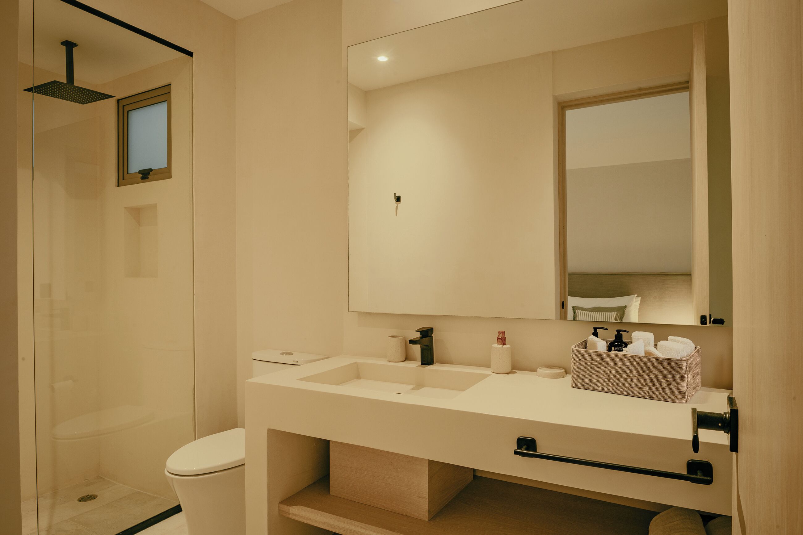 Une salle de bain moderne avec un grand miroir, un lavabo agrémenté d’un panier contenant des articles de toilette et un espace douche.