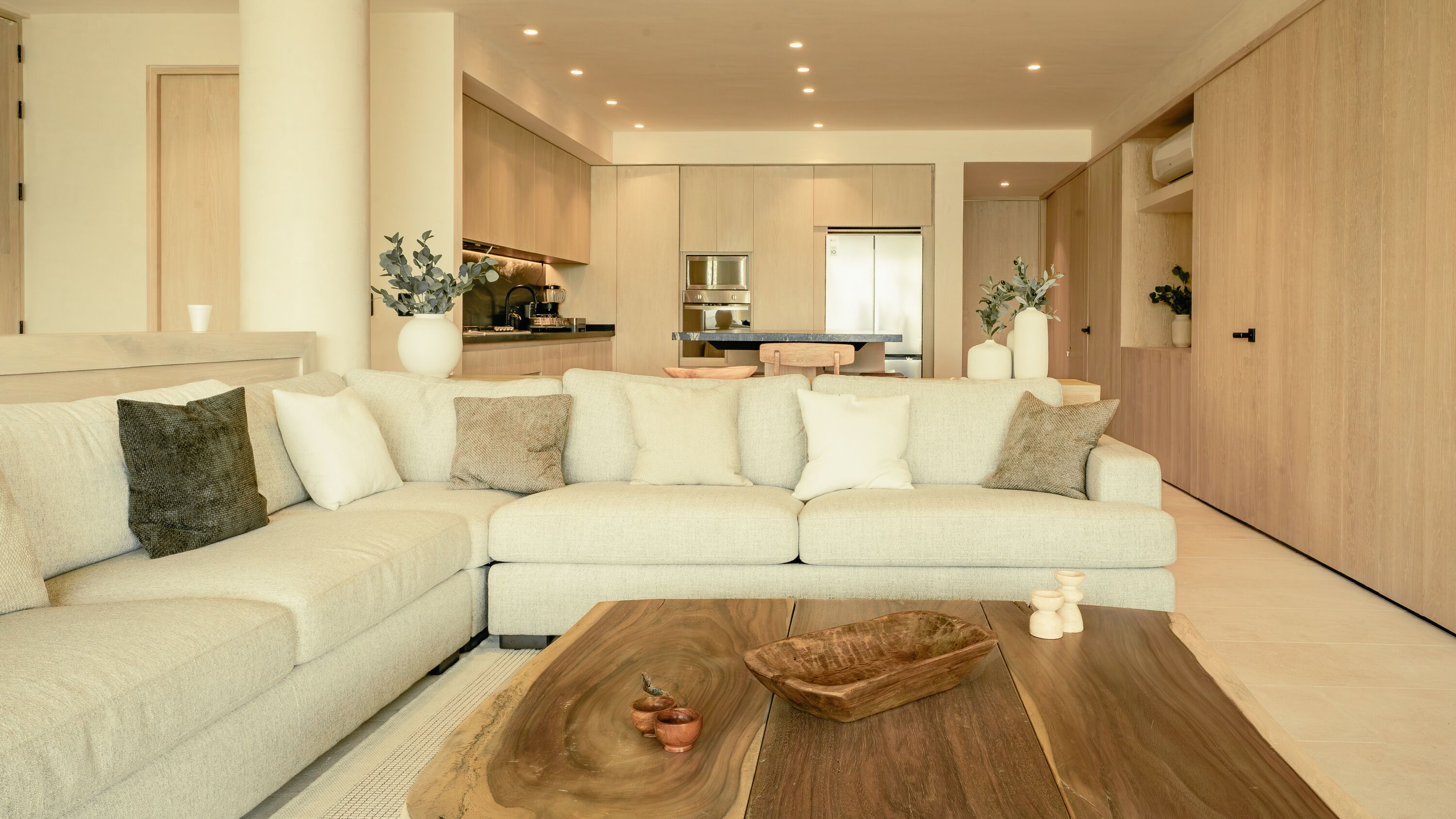 A modern living room with a sectional sofa, a wooden coffee table, and a kitchen in the background.