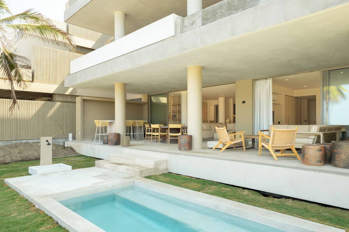 A modern outdoor pool area with a two-story building, outdoor seating, and a palm tree.