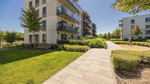 A modern multi-story residential building with balconies, a paved walkway, and well-maintained landscaping.