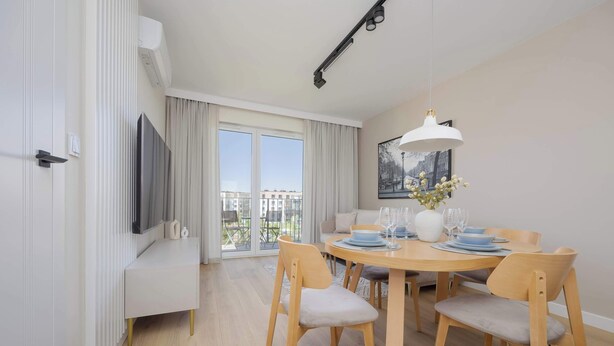 A modern dining area with a round wooden table, six chairs, and a white pendant light.
