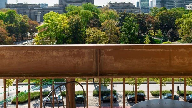 Un balcon offrant une vue sur le paysage urbain, avec notamment un bâtiment imposant surmonté d’une flèche.