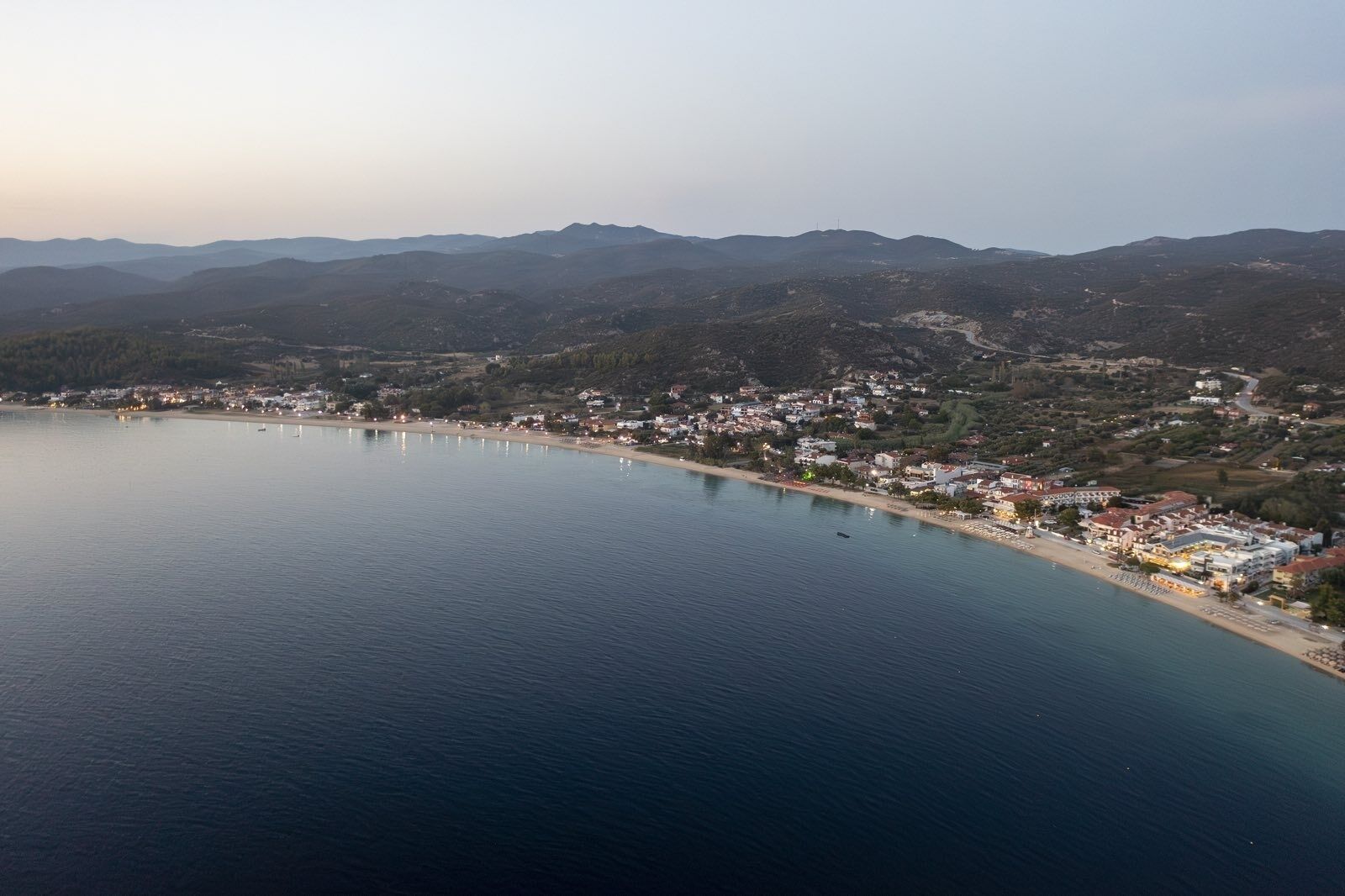 An aerial view of a coastal town with a beach, houses, and mountains in the background.