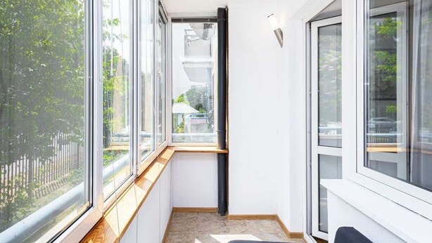 Una habitación estrecha con ventanas amplias, un banco de madera y una silla negra.