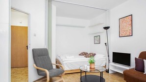 Una habitación moderna con una cama, un sofá, una silla, un televisor y una mesita con una planta.