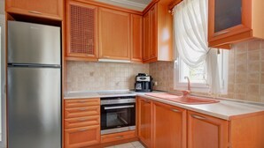 A kitchen with wooden cabinets, a stainless steel refrigerator, a built-in oven, a coffee maker, and a window with curtains.