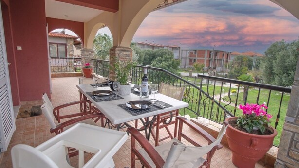 A covered patio with a table set for dining, surrounded by chairs, and overlooking a residential area with a view of the sky.
