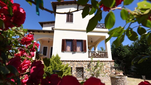 A two-story house with a stone foundation, a balcony, and a garden with red roses. - Azalia House by Rentalspro (Nea Propontida)