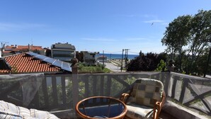 A patio with wicker furniture and a glass table, overlooking a coastal area with buildings and a view of the sea. - Azalia House by Rentalspro (Nea Propontida)