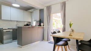 A modern kitchen with grey cabinets, a dishwasher, and a dining area with a wooden table and black chairs. - Artistic Vibe by Rentalspro - Nikiti Halkidiki (Sithonia)