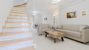 A modern living room with a staircase, a sofa, a coffee table, and artwork on the walls. - Artistic Vibe by Rentalspro - Nikiti Halkidiki (Sithonia)