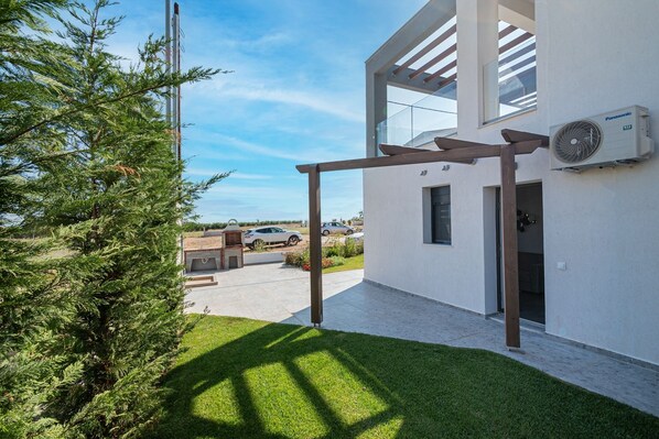 A modern building with a white exterior, a pergola, and a Panasonic air conditioning unit.